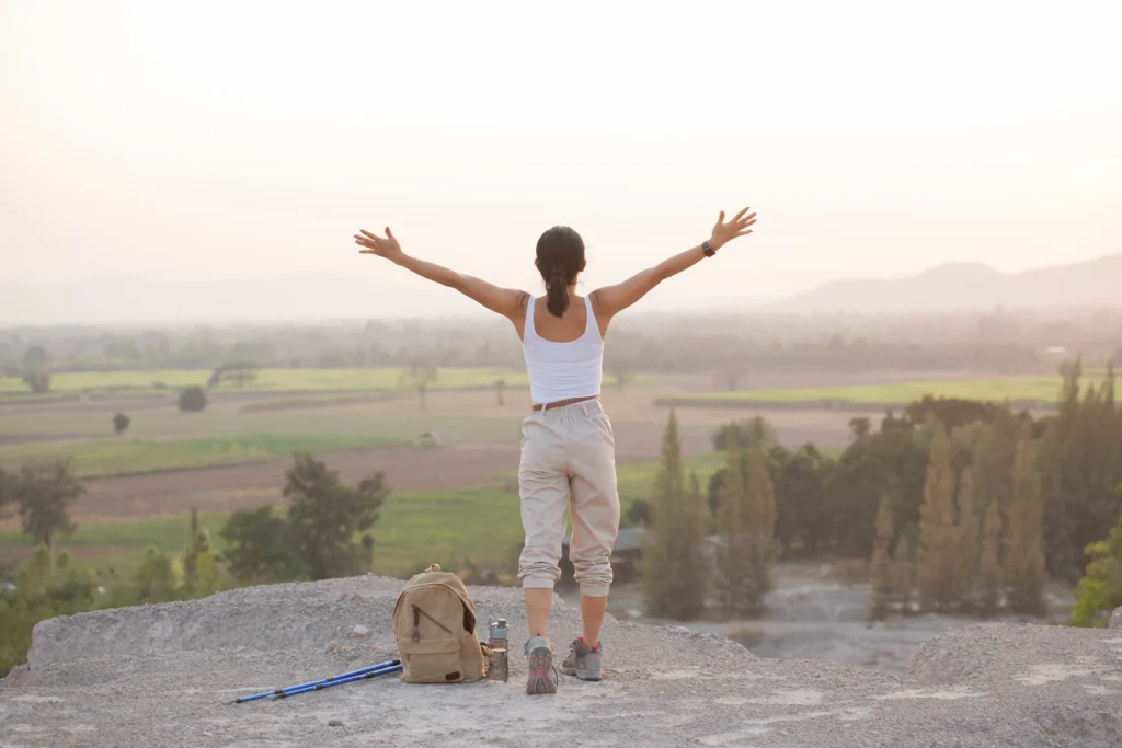 woman-raising-hands-up-top-mountain-while-hiking-poles-standing-rocky-mountain-ridge-looking-out-valleys